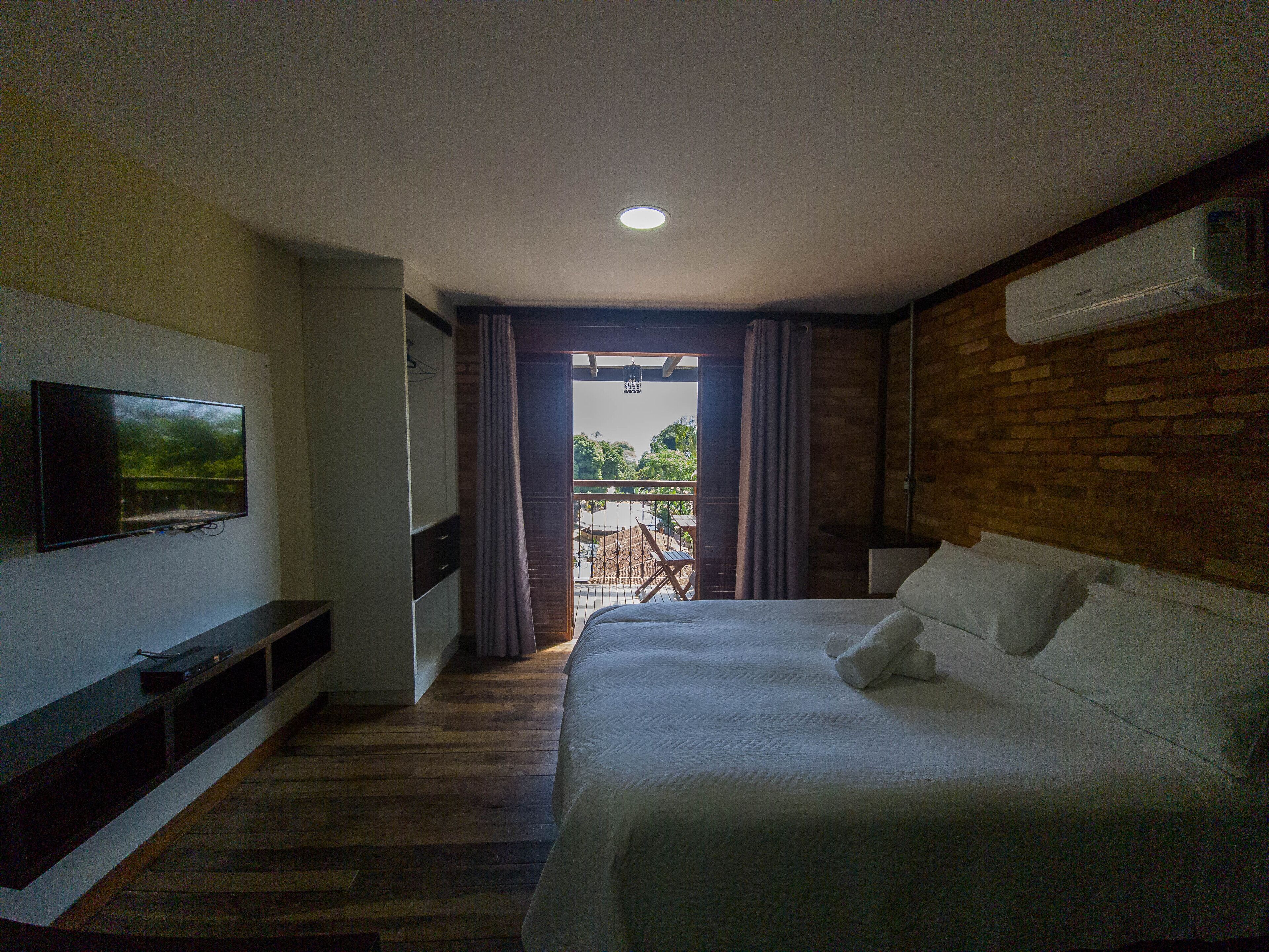 Een hotelkamer met een bed, een aan de muur bevestigde televisie en een balkon met gordijnen.