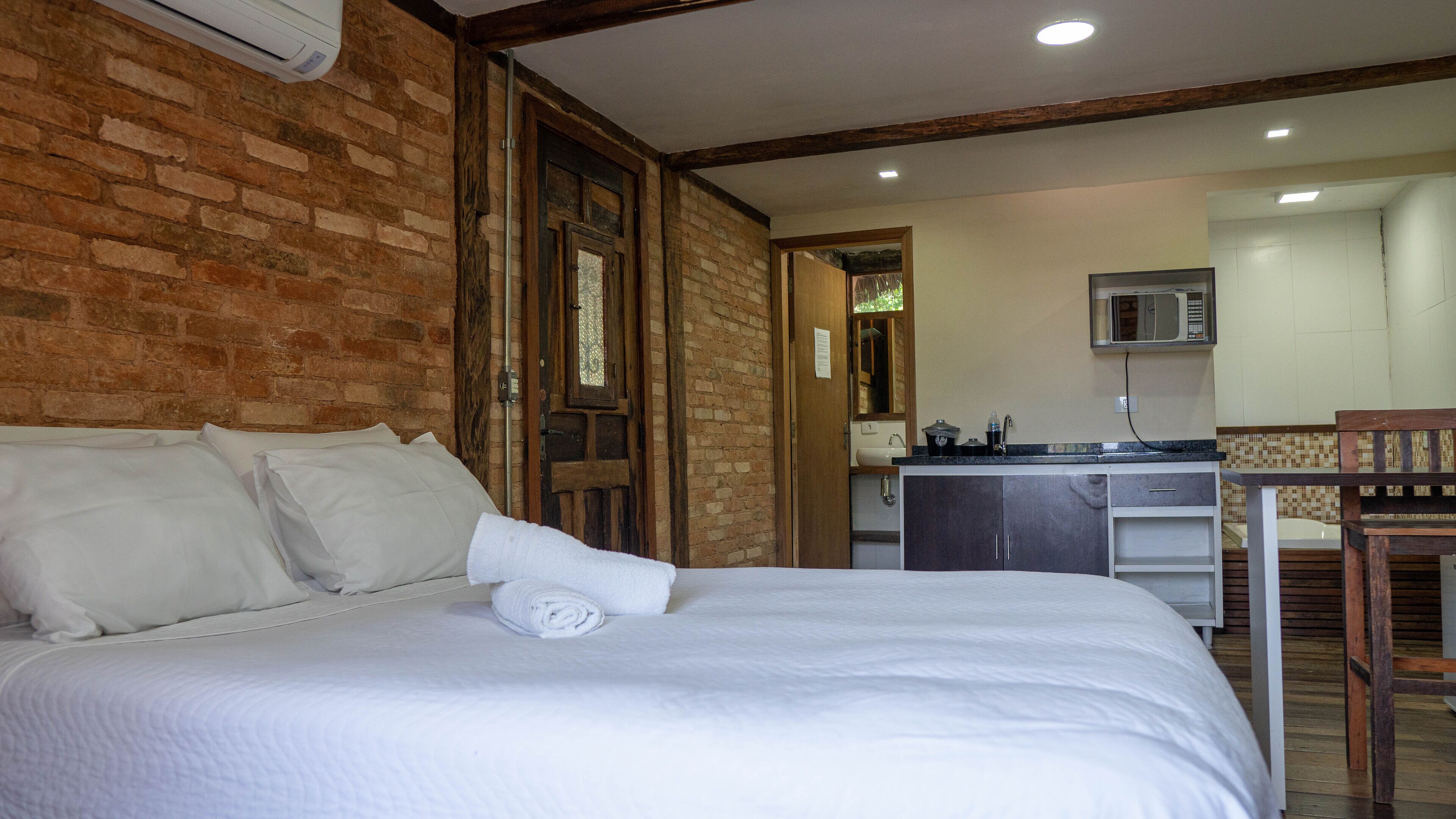 A bedroom with a bed, a wooden door, a brick wall, and a kitchenette with a microwave.