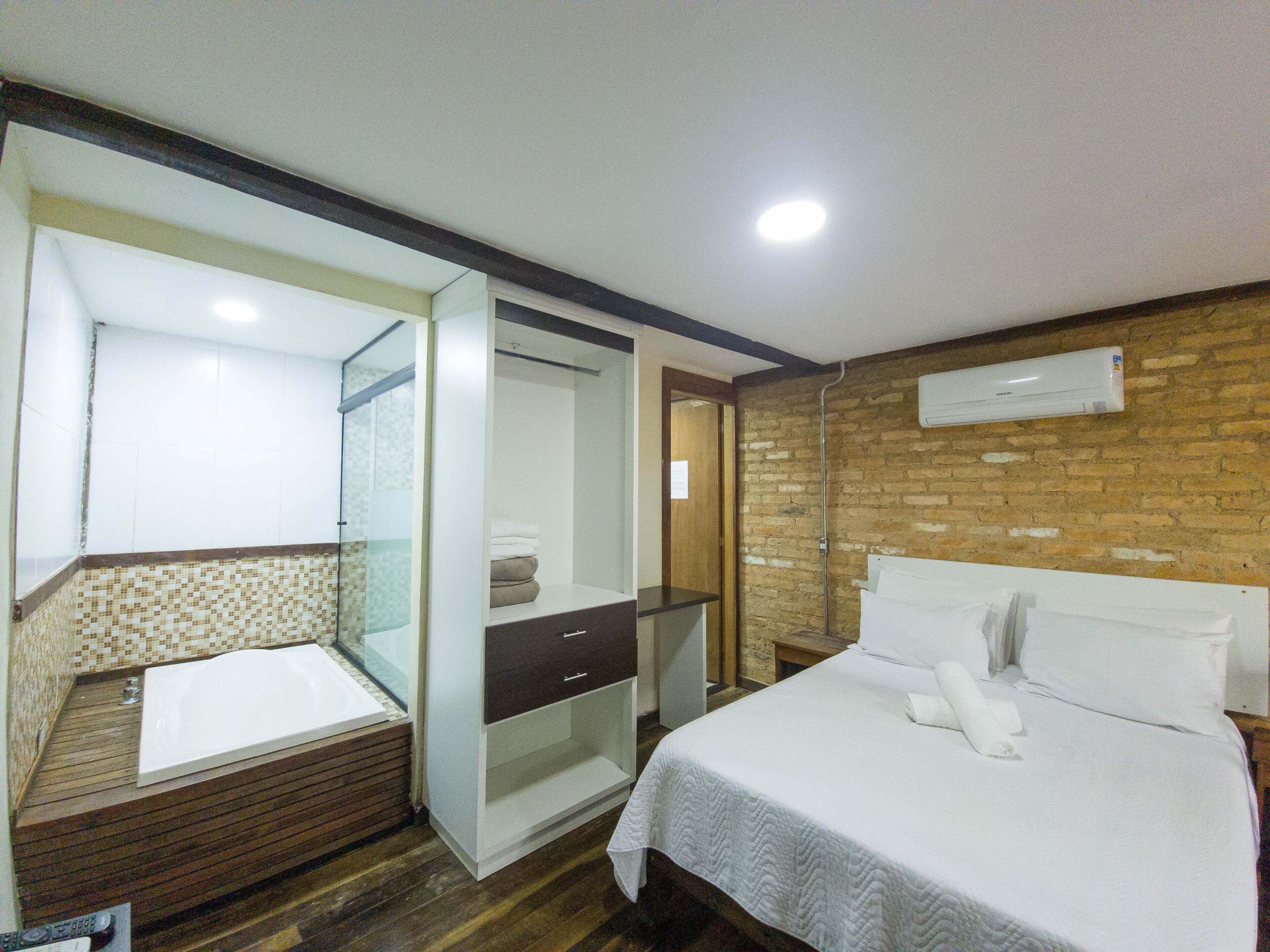 A hotel room with a bed, a bathroom with a glass shower enclosure, and a brick wall.