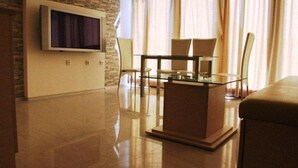 A modern living room with a flat-screen TV mounted on a brick wall, a glass coffee table, and a beige sofa. - Villa Itta (Sunny Beach)