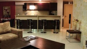 A modern living room with a sofa, a coffee table, and a kitchen area with bar stools. - Villa Itta (Sunny Beach)