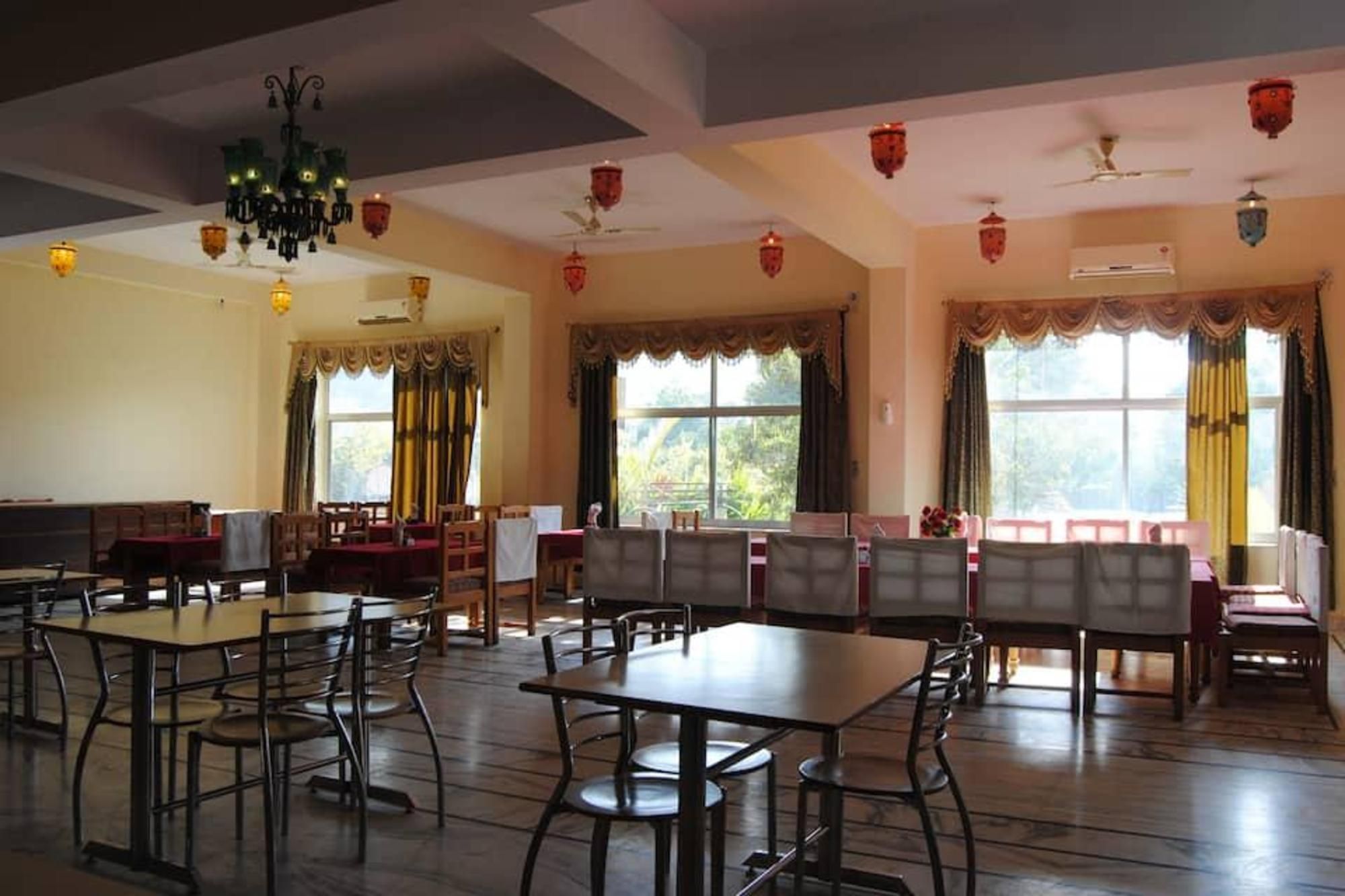 Uma sala de jantar com mesas e cadeiras, janelas amplas com cortinas e ventiladores de teto.