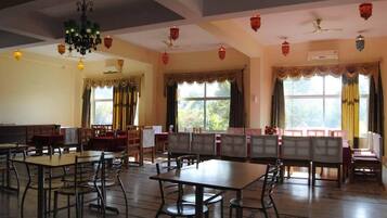 Uma sala de jantar com mesas e cadeiras, janelas amplas com cortinas e ventiladores de teto.