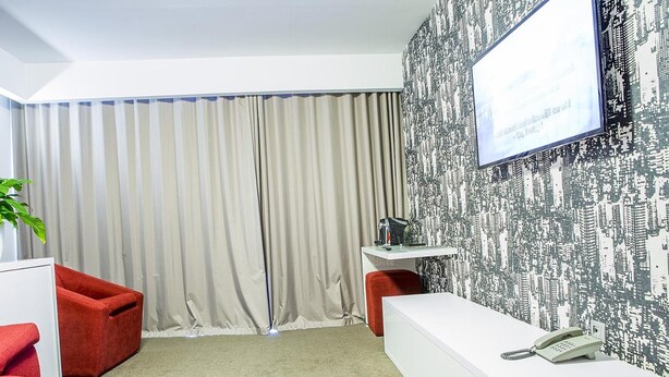 A hotel room with a large window, a white desk with a telephone, a red chair, and a plant. - Tempo Hotel Targu Mures (Tirgu Mures)