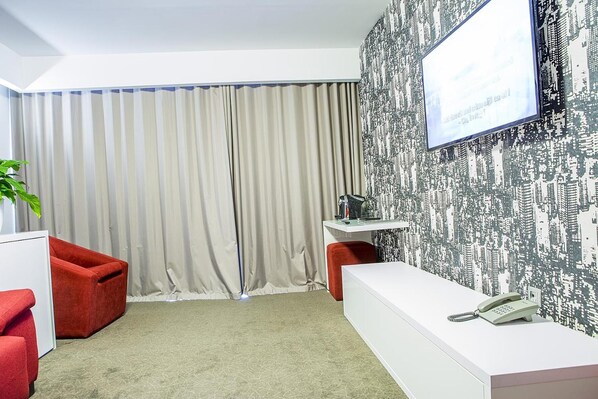 A hotel room with a large window, a white desk with a telephone, a red chair, and a plant. - Tempo Hotel Targu Mures (Tirgu Mures)