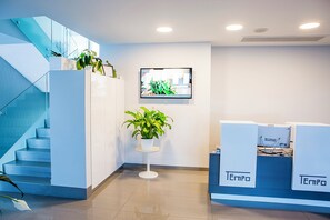 A reception area with a staircase, potted plants, and a computer monitor on the wall.