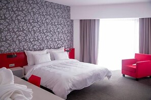 A hotel room with a large bed, a red armchair, and a patterned wall.
