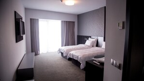 A hotel room with two beds, a flat-screen TV, a bedside table, and a large window with curtains. - Tempo Hotel Targu Mures (Tirgu Mures)