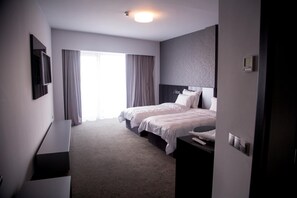 A hotel room with two beds, a flat-screen TV, a bedside table, and a large window with curtains. - Tempo Hotel Targu Mures (Tirgu Mures)