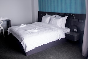 A modern hotel room with a large bed, a bedside table, a chair, and a nightstand.