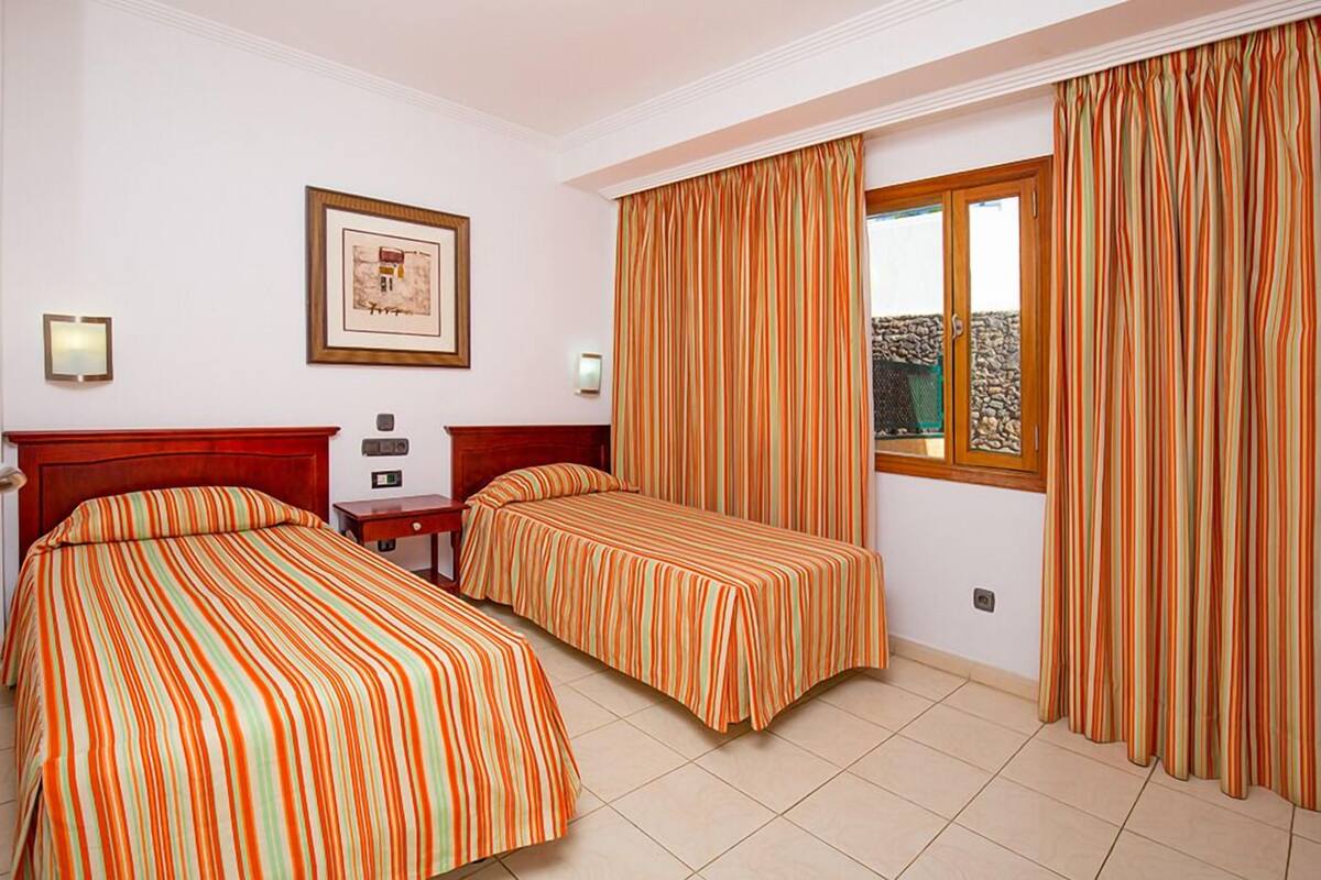 A hotel room with two beds, a wooden headboard, a framed picture on the wall, and a window with curtains.