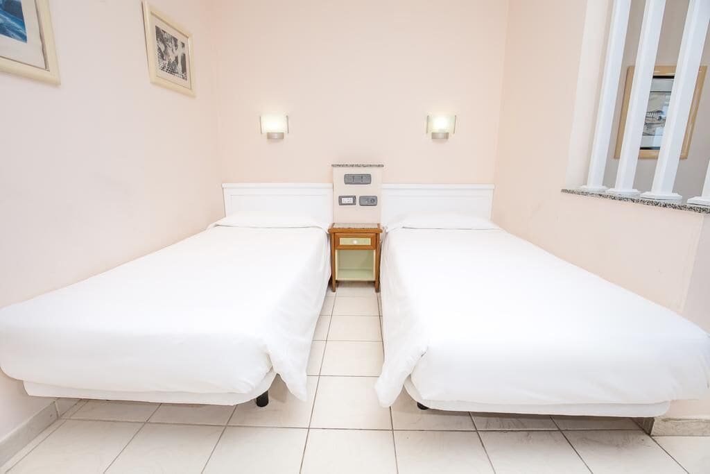 Habitación doble con dos camas individuales, una mesita de noche con lámpara y un calentador de pared.