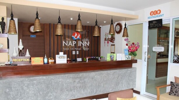 A reception area with a wooden counter, multiple hanging pendant lights, and a reception desk. - Nap Inn (Ko Pha-ngan)