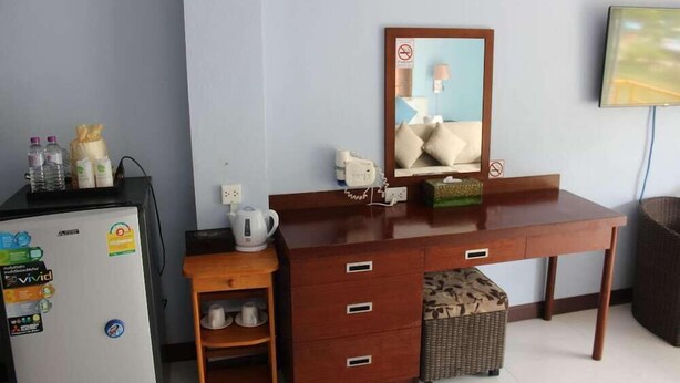 A hotel room with a wooden desk, a refrigerator, a microwave, a kettle, a basket, and a television. - Nap Inn (Ko Pha-ngan)