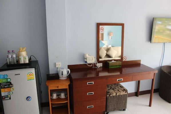A hotel room with a wooden desk, a refrigerator, a microwave, a kettle, a basket, and a television. - Nap Inn (Ko Pha-ngan)