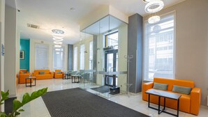 Eine moderne Lobby mit orangefarbenen Sitzgelegenheiten, Glaswänden und einer zentralen Treppe.