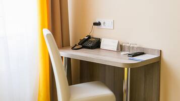 A hotel desk with a telephone, a glass of water, and a remote control.