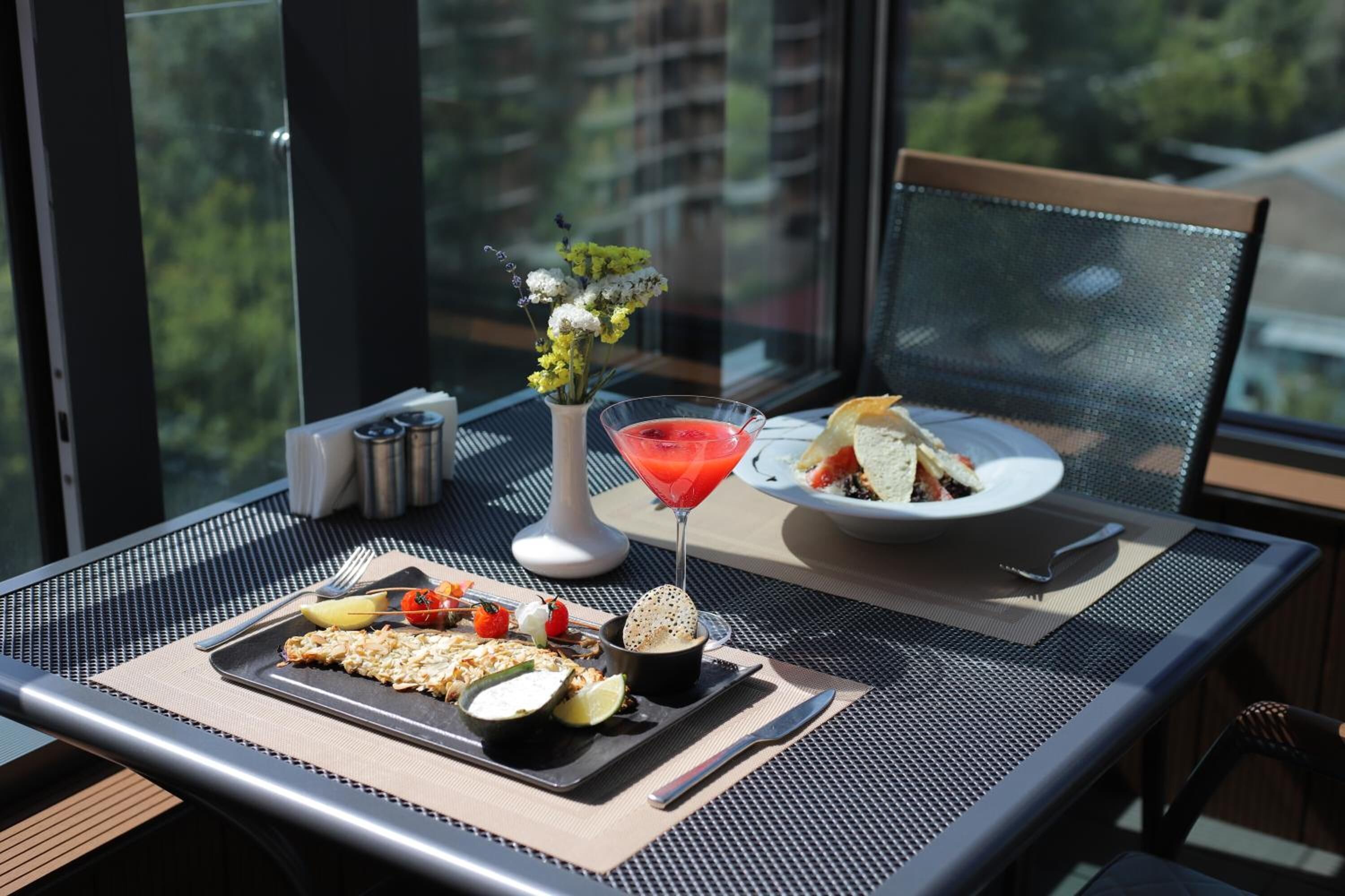 A dining table with a meal, a martini glass, and a vase of flowers.