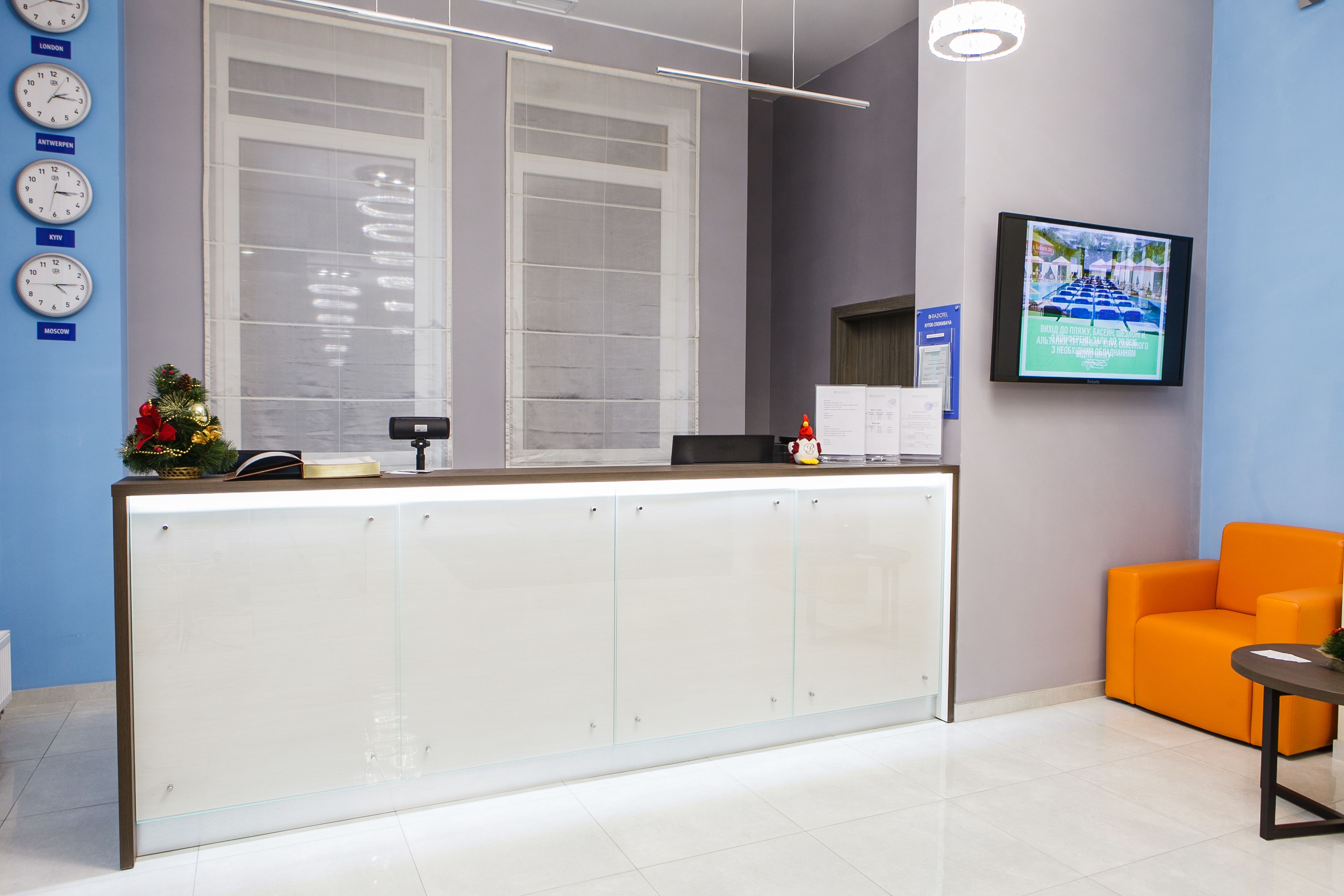 A reception area with a modern desk, a large window, a TV screen, and a clock on the wall.