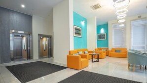 Eine moderne Lobby mit zwei Aufzügen, einer orangefarbenen Sitzgelegenheit und einer blauen Akzentwand.