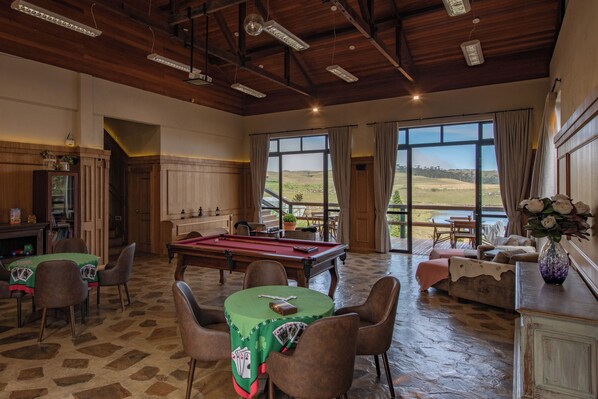 A room with a pool table, billiards, a green table with playing cards, a sofa, and a view of the outdoors. - Rio do Rastro Eco Resort (Bom Jardim da Serra)