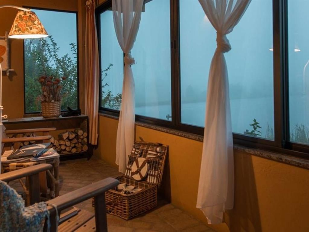 Una habitación acogedora con un ventanal grande, una lámpara, una cesta de mimbre y una mesa con un ordenador portátil.
