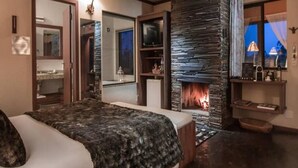 Une chambre avec un grand lit, une cheminée en pierre, un téléviseur et un miroir.