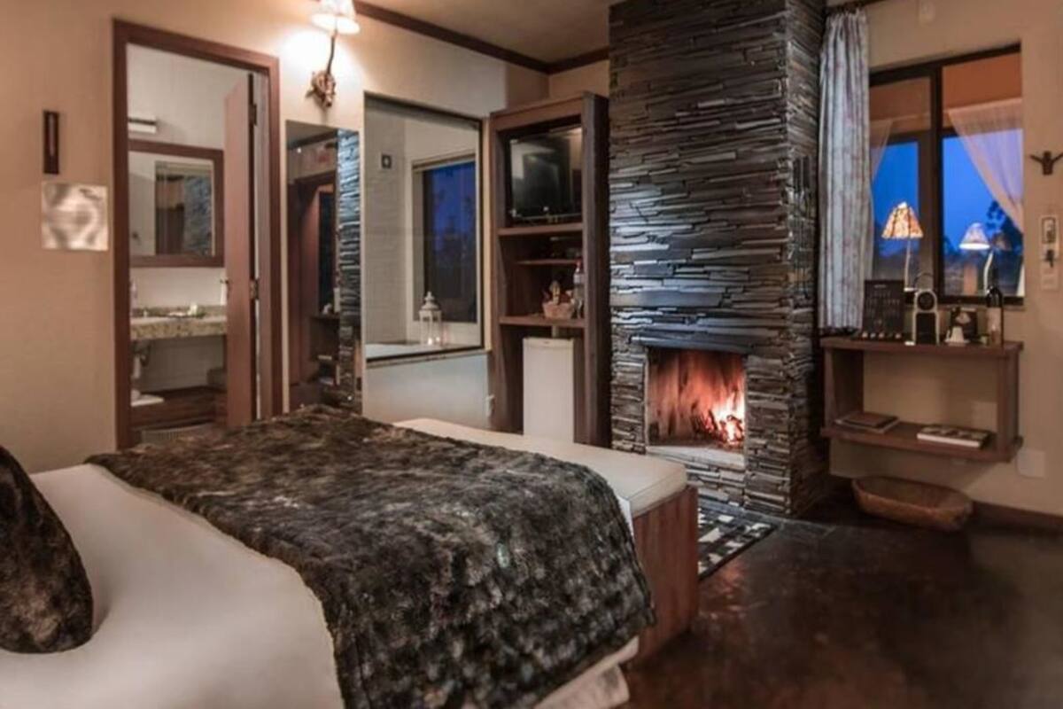 Une chambre avec un grand lit, une cheminée en pierre, un téléviseur et un miroir.