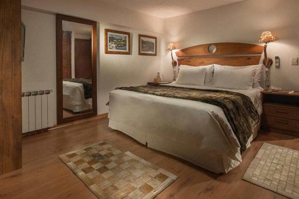 Une chambre à coucher avec une tête de lit en bois, un lit recouvert de draps blancs, une table de chevet avec une lampe et un tapis à carreaux.