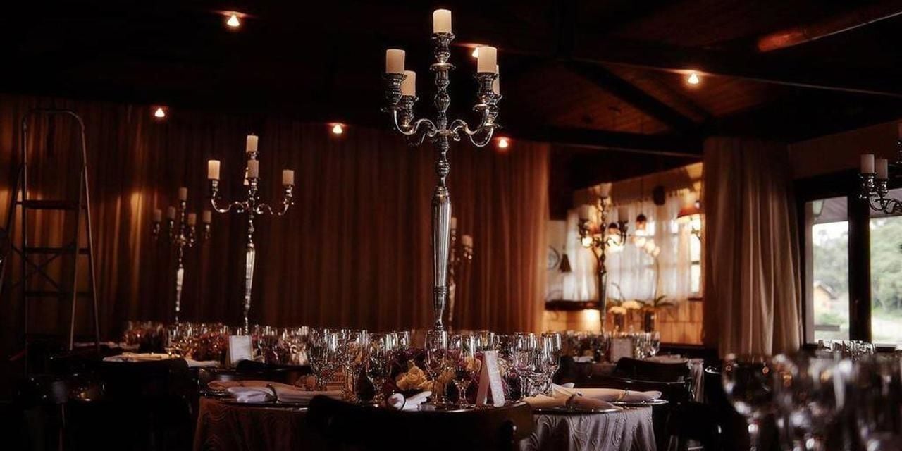 A dimly lit dining area with multiple tables set for a meal, each with a candelabra centerpiece.