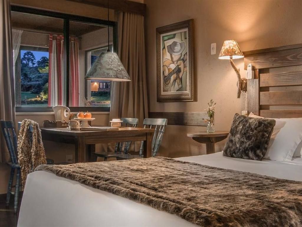 Una habitació d'hotel amb un llit gran, una taula de menjador, cadires, una làmpada i un quadre a la paret.