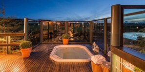 A wooden deck with a hot tub, glass walls, and potted plants.