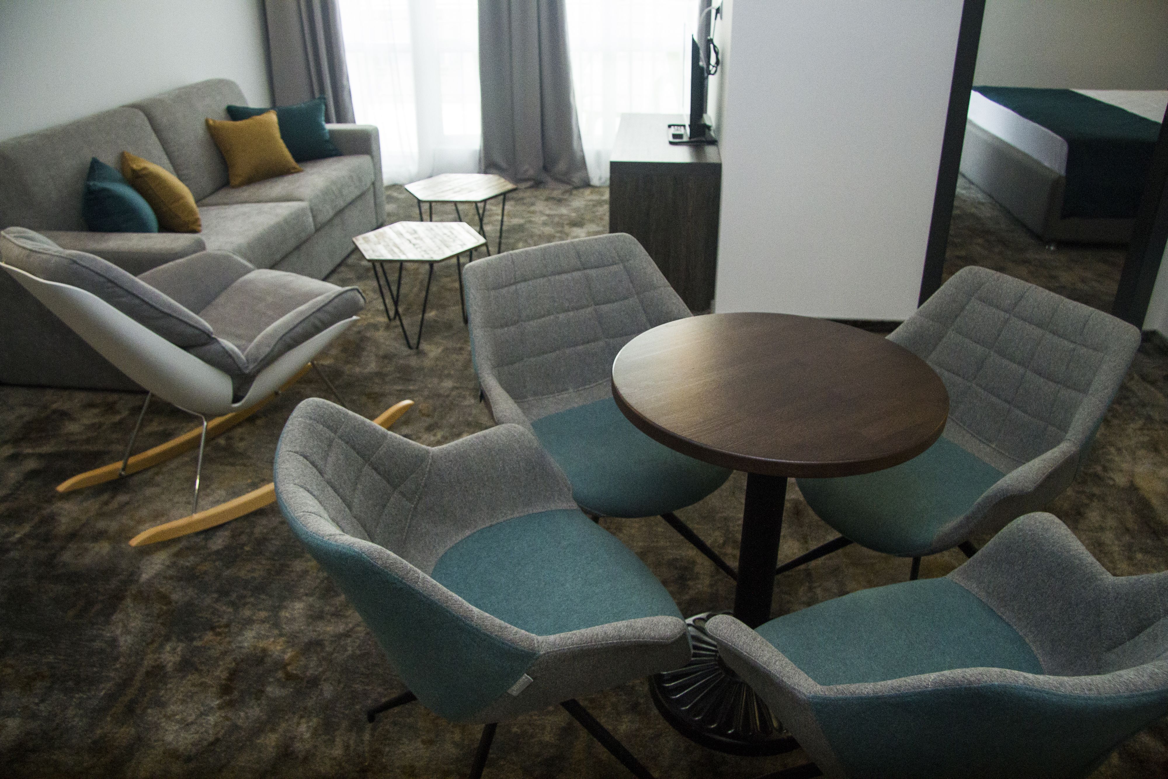 A modern living room with a grey sofa, teal armchairs, a small round table, and a coffee table.
