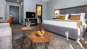 A hotel room with a bed, a TV, a seating area with a sofa and armchair, a small table with a fruit bowl, and a mirror. - Best Western Plus Premium Inn (Sunny Beach)