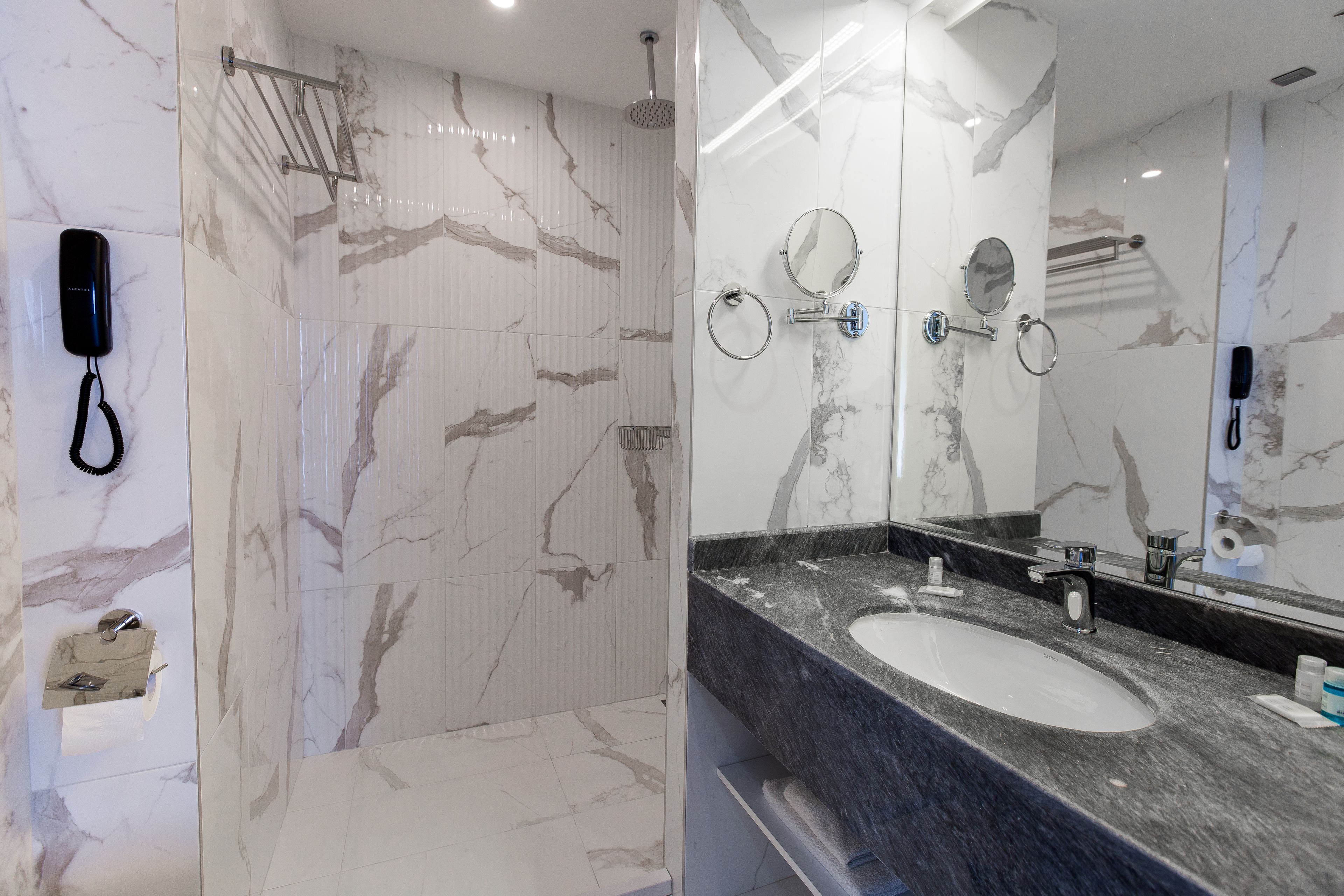 Een badkamer met een marmeren douche, een wastafel met spiegel en een handdoekhouder.