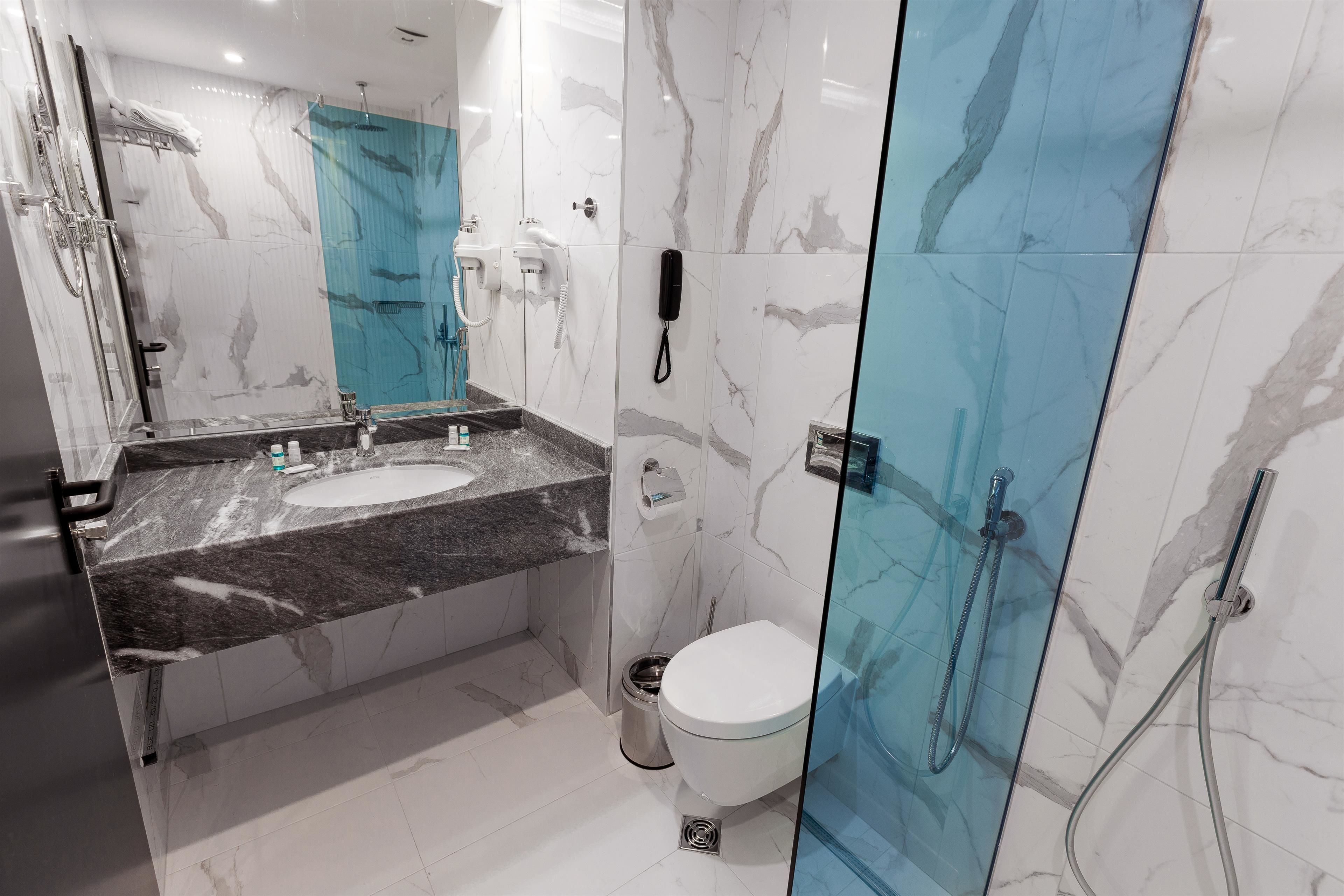 A modern bathroom with a marble sink, a glass shower enclosure, and a toilet.