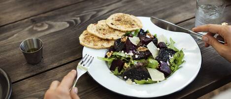 A wooden table with a plate of salad, a glass of water, and a metal cup.