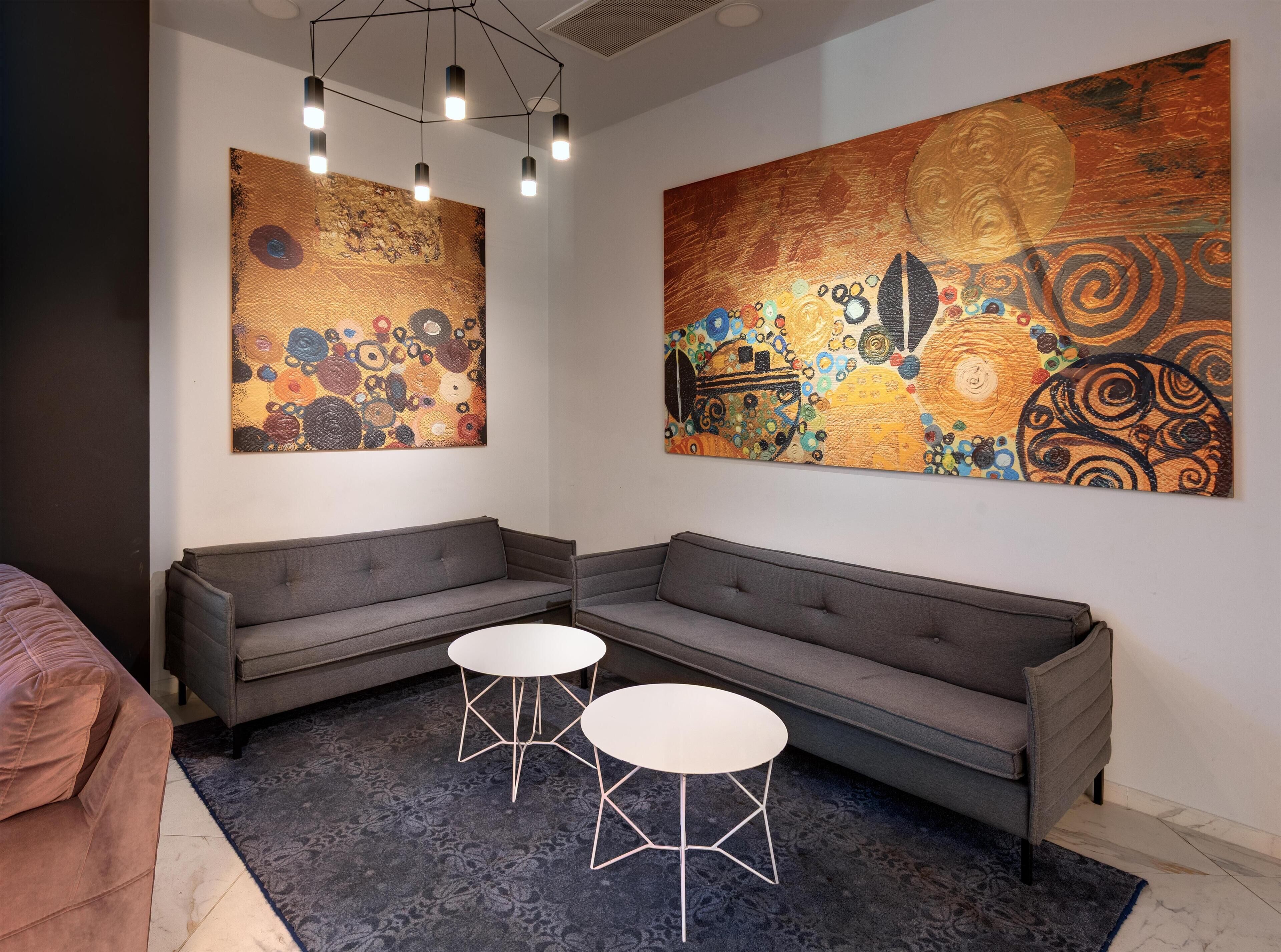 A modern room with a grey sofa, two white tables, and large abstract paintings on the walls.