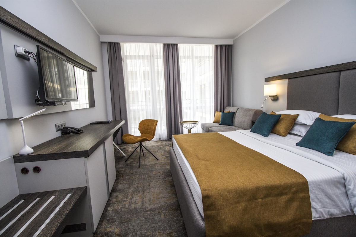 A hotel room with a bed, a desk, a chair, a TV, and a window with curtains.