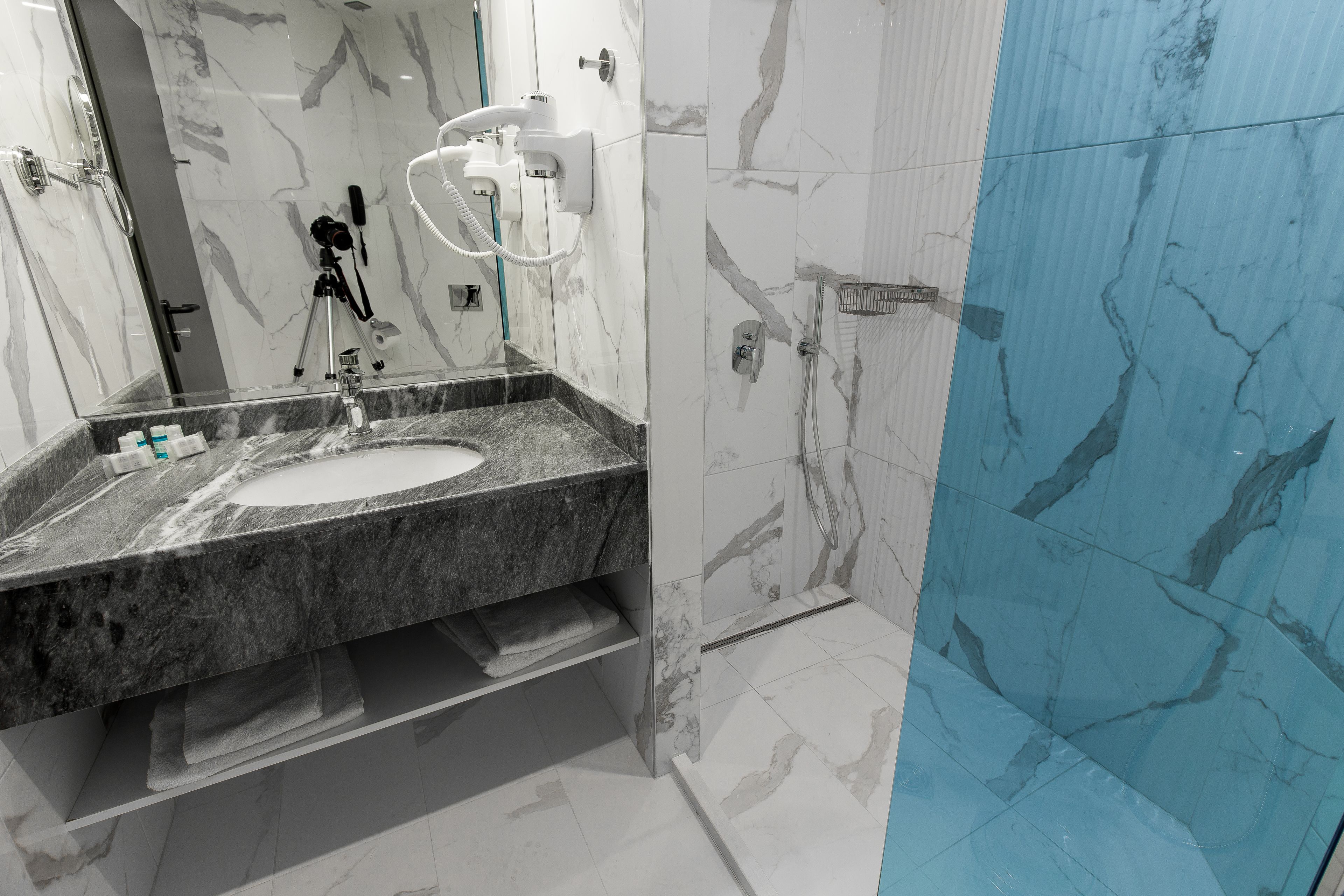 A modern bathroom with a marble sink, a handheld showerhead, and a towel rack.