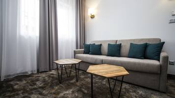 En moderne stue med en grå sofa, to træsideborde og turkise puder.