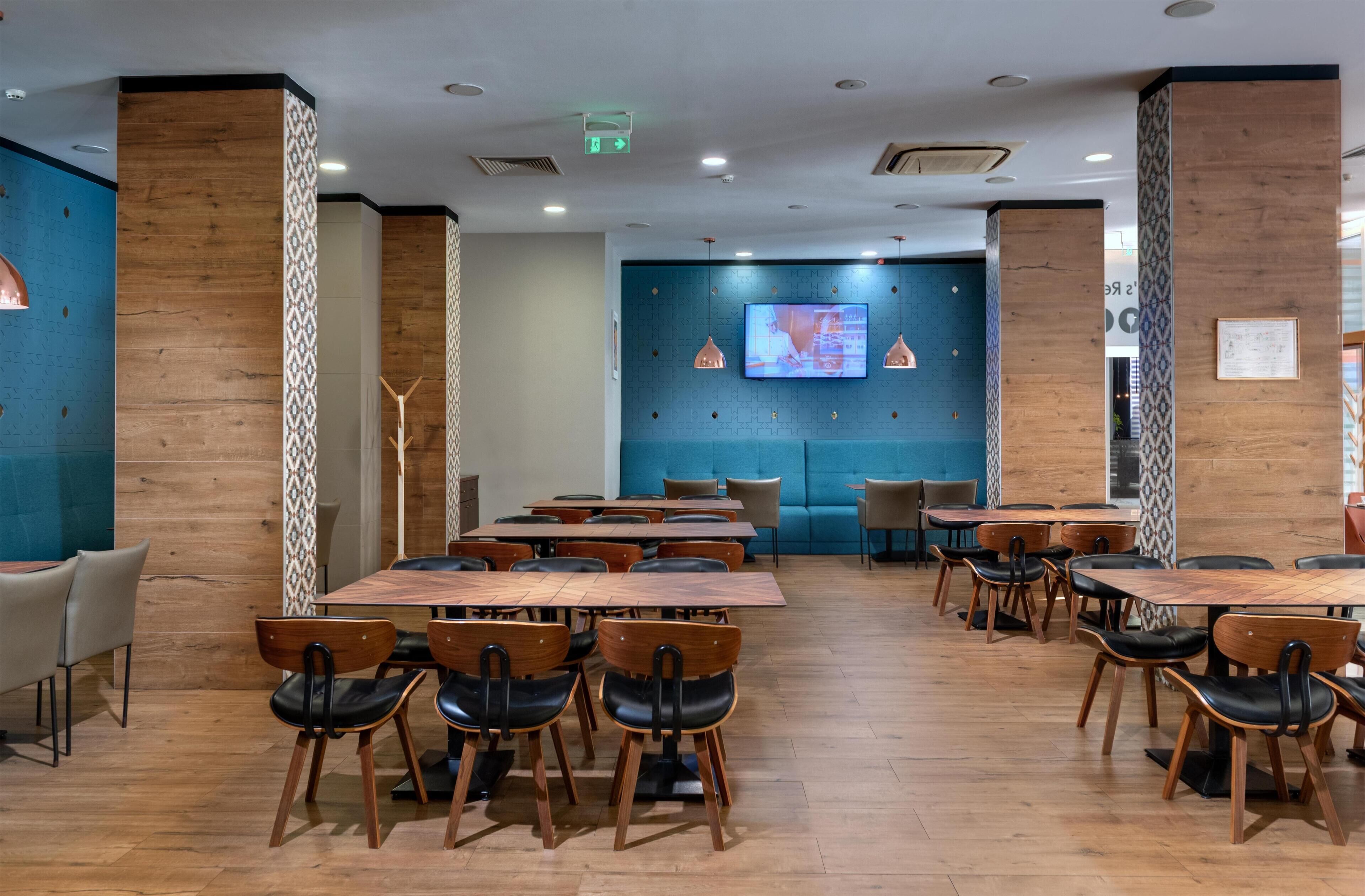 Un espace de restauration moderne avec des tables et des chaises en bois, un mur d’accent bleu et des luminaires suspendus.