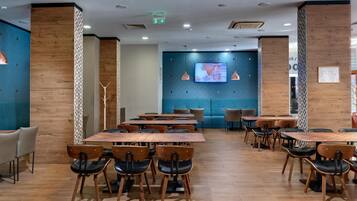 Un espace de restauration moderne avec des tables et des chaises en bois, un mur d’accent bleu et des luminaires suspendus.