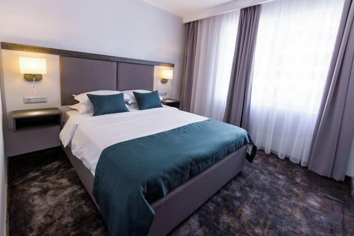 A hotel room with a large bed, two bedside tables, and a window with curtains.