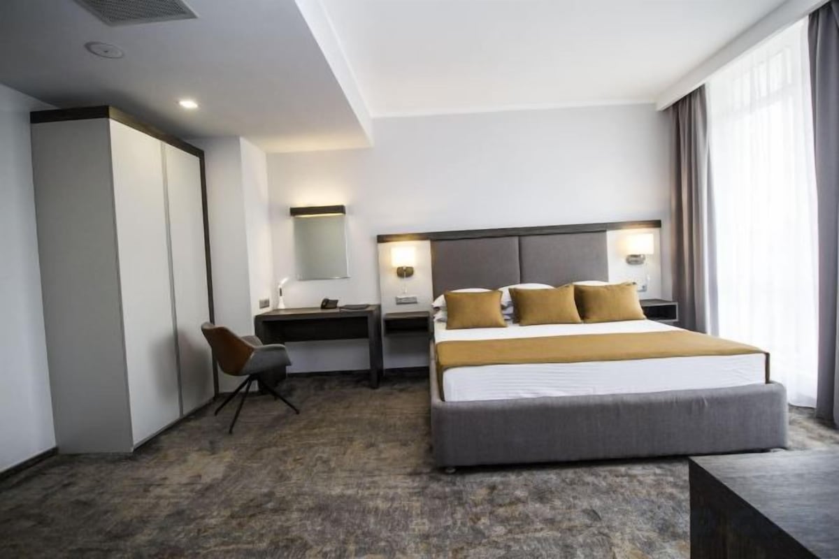 A hotel room with a bed, desk, chair, and a large window.