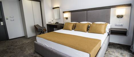 A hotel room with a large bed, a desk, a chair, a wardrobe, and two wall-mounted lamps.