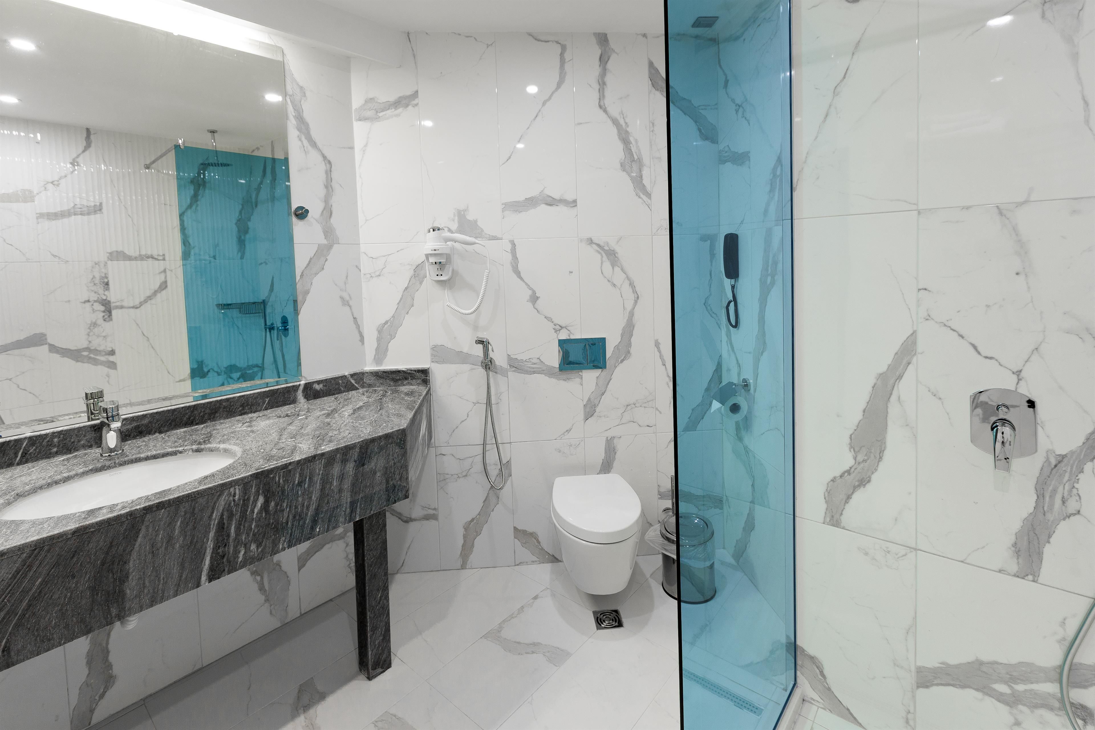 Un baño moderno con tocador de mármol, cabina de ducha de vidrio y un inodoro blanco.