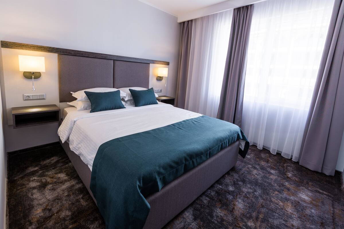 A hotel room with a large bed, two bedside tables, and a window with curtains.