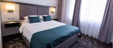 A hotel room with a large bed, two bedside tables, and a window with curtains.