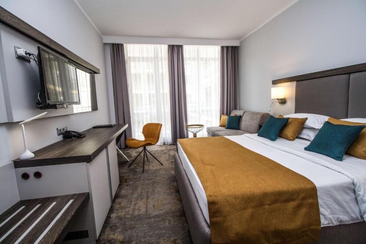 A hotel room with a bed, a desk, a chair, a TV, and a window with curtains.